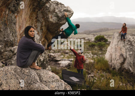 Portrait of woman sitting on rock with friends in background Stock Photo
