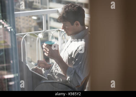 Man using digital tablet while having cup of coffee in balcony Stock Photo