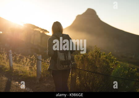 Rear view of female hiker with backpack walking on mountain during sunset Stock Photo