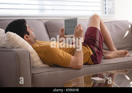 Man using digital tablet on sofa in living room at home Stock Photo