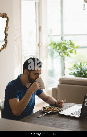 Man using laptop while having breakfast at home Stock Photo