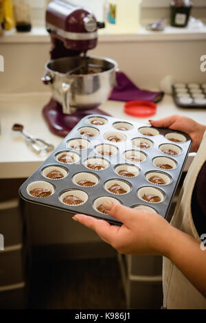Woman holding baking tray with cupcakes in the kitchen Stock Photo