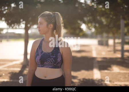 Young woman looking away while standing in park during sunny day Stock Photo