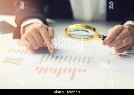 business women using magnifying glass to review financial summary chart report. auditing concept Stock Photo