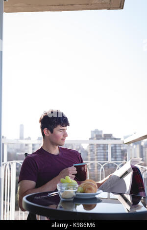 Man reading newspaper while having cup of coffee in balcony Stock Photo