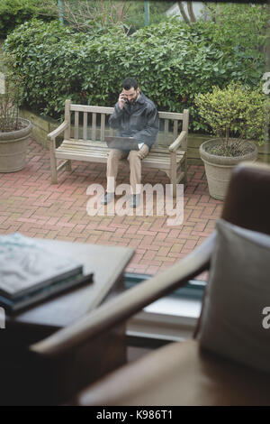 Man talking on mobile phone while working on laptop in the garden Stock Photo