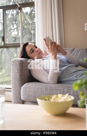 Young woman using smart phone while lying on sofa at home Stock Photo