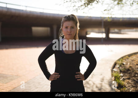 Portrait of young woman with hands on hip standing against bridge on street Stock Photo