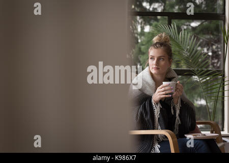 Thoughtful woman having coffee while sitting on chair at home Stock Photo