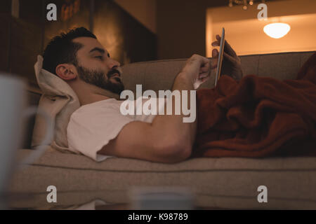 Man using digital tablet while lying on sofa in the living room at home Stock Photo