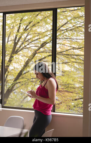 Side view of woman using tablet computer while standing by window at home Stock Photo