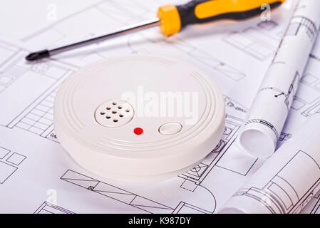Smoke detector lying on blueprints with screwdriver in the background Stock Photo