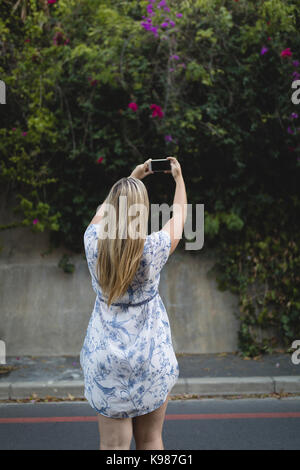 Rear view of young woman photographing with mobile phone while standing on road Stock Photo