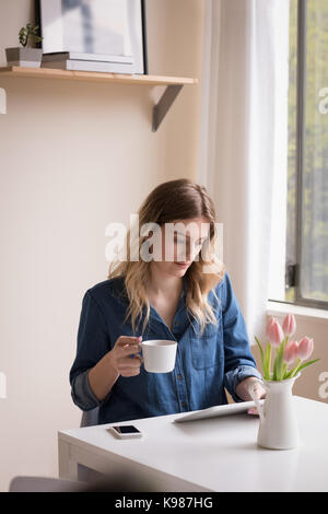 Woman having coffee while using digital tablet at table Stock Photo