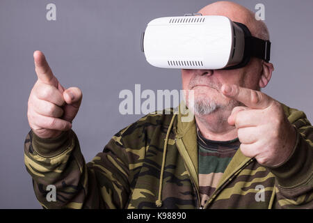 Senior man in wearable technology VR glasses. Confident old man wearing camouflage clothing in virtual reality headset with Interface selective focus  Stock Photo