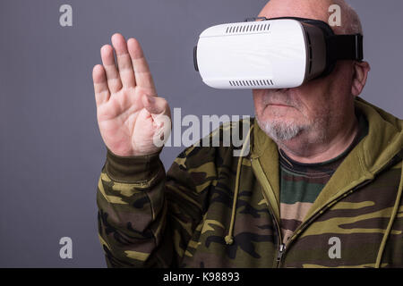 Senior man in wearable technology VR glasses. Confident old man wearing camouflage clothing in virtual reality headset with Interface selective focus  Stock Photo