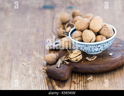 Walnuts in ceramic bowl and on cutting board with nutcracker over  rustic wooden background Stock Photo