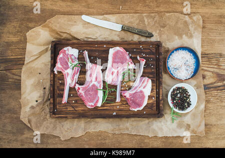 Rack of Lamb with rosemary and spices on rustic chopping board over oily craft paper, old wooden background Stock Photo