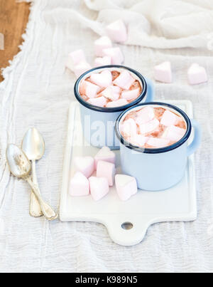 Saint Valentine's holiday greeting set. Hot chocolate and heart shaped marshmallows in old enamel mugs on white ceramic serving board  Stock Photo