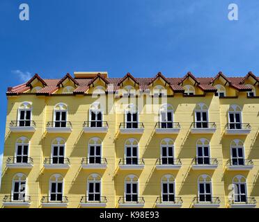 Classical facade of a mansion in Singapore with bright yellow exterior, iron balconies and dramatic shadows set against a deep blue tropical sky Stock Photo