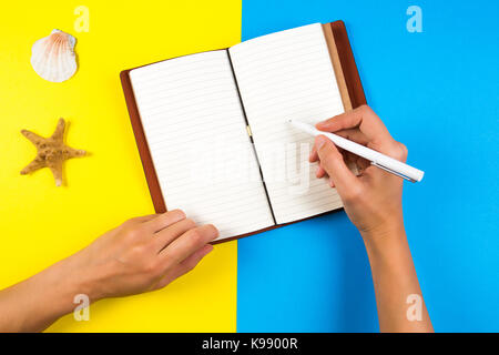 Travel, vacation, summer concept. Woman hand writing in notebook over blue and yellow background Stock Photo
