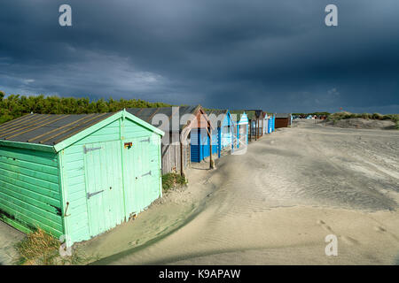 Dark storm clouds gather over colourful beach huts at West Wittering on the West Sussex coast Stock Photo