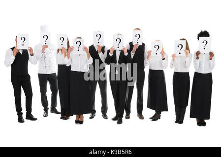 Full length of restaurant staff hiding faces with question mark signs against white background Stock Photo