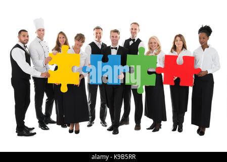 Portrait of confident restaurant staff joining jigsaw pieces against white background Stock Photo