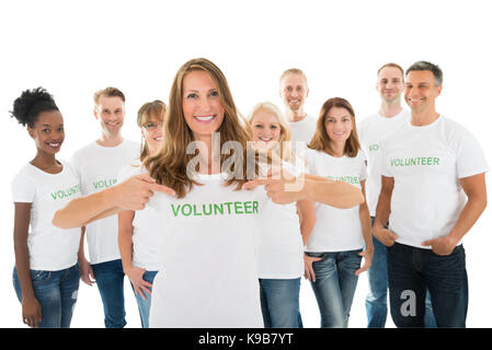 Portrait of happy woman showing volunteer text on tshirt with friends standing over white background Stock Photo