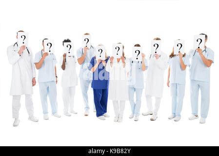 Full length of multiethnic medical team covering faces with question mark signs against white background Stock Photo