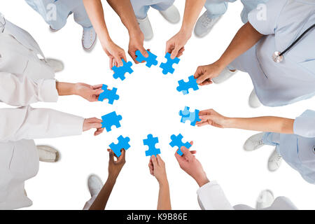 Directly above shot of medical team holding blue jigsaw pieces in huddle against white background Stock Photo
