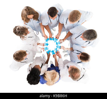 Directly above shot of medical team joining blue jigsaw pieces against white background Stock Photo