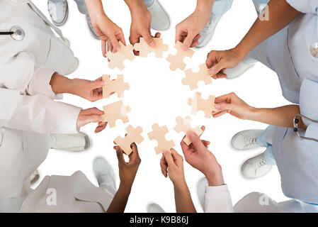 Directly above shot of medical team holding blue jigsaw pieces in huddle against white background Stock Photo