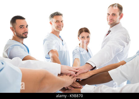 Portrait of smiling medical team piling hands while standing against white background Stock Photo