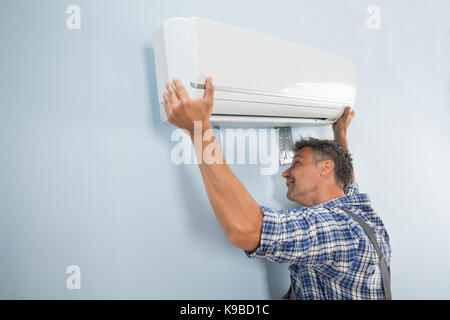 Portrait Of A Mid-adult Male Technician Fixing Air Conditioner On Wall Stock Photo
