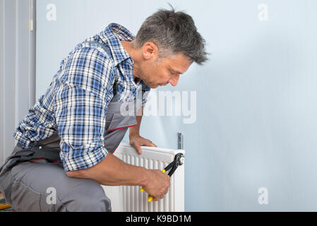 Portrait Of Male Plumber Fixing Radiator With Wrench Stock Photo