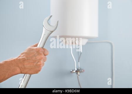 Close-up Of A Person's Hand Holding Spanner In Front Of Electric Boiler Stock Photo