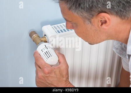 Man Adjusting Temperature Of Radiator Using Thermostat Stock Photo