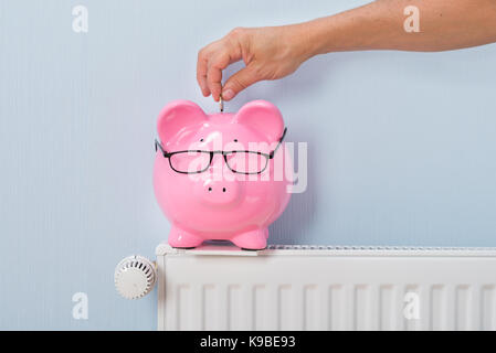 Close-up Of Ma's Inserting Coin In Piggy Bank Kept On Radiator Stock Photo