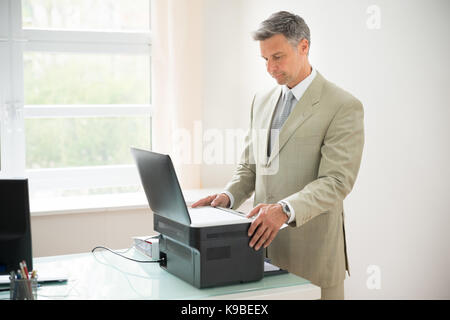 Mid-adult Businessman Using Photocopy Machine In Office Stock Photo