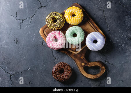 Variety of colorful glazed donuts on wooden serving board over black texture background. Top view with space Stock Photo