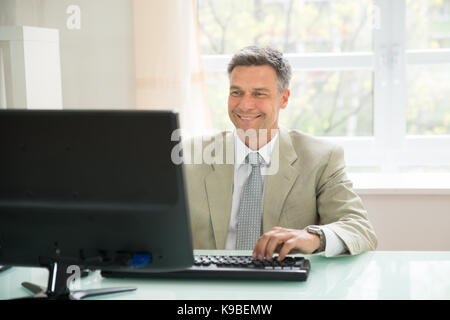 Portrait Of Happy Businessman Using Office Computer Stock Photo