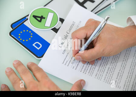 Close-up Of A Person Filling Car Sale Contract Form With Number Plate On Desk. Contract Paper Contains Placeholder Text Stock Photo