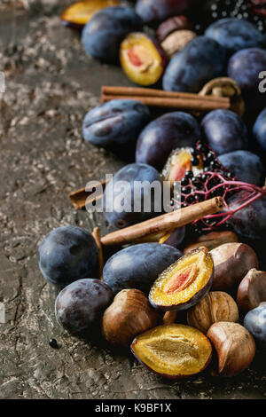 Autumn plums, nuts, cinnamon over brown concrete background. Close up with space for text. Fall harvest and jam making concept. Stock Photo