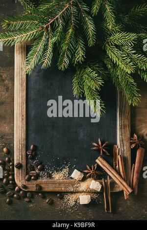 Vintage empty chalkboard with fir Christmas tree, coffee beans, spices, brown sugar over wooden background. Top view with space for text Stock Photo