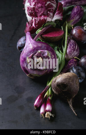 Assortment raw organic of purple vegetables mini eggplants, spring onion, beetroot, radicchio salad, plums, kohlrabi, flower salt over dark metal back Stock Photo