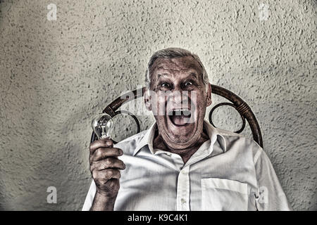 emotional old man holding a light bulb and thinking and finding solution to problem Stock Photo