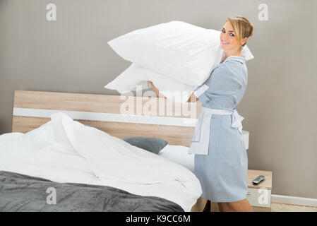 Happy Female Housekeeping Worker With Pillows In Hotel Room Stock Photo