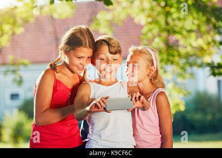 Happy children taking a selfie with smart phone. Themes friendship, summertine and modern technology Stock Photo