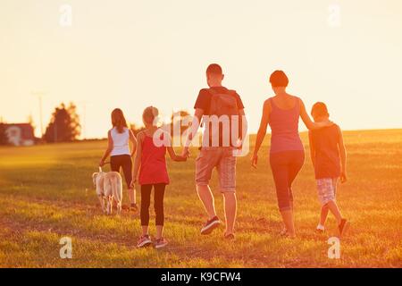 Summertime in the countryside. Silhouettes of the family with dog on the trip at the sunset. Stock Photo